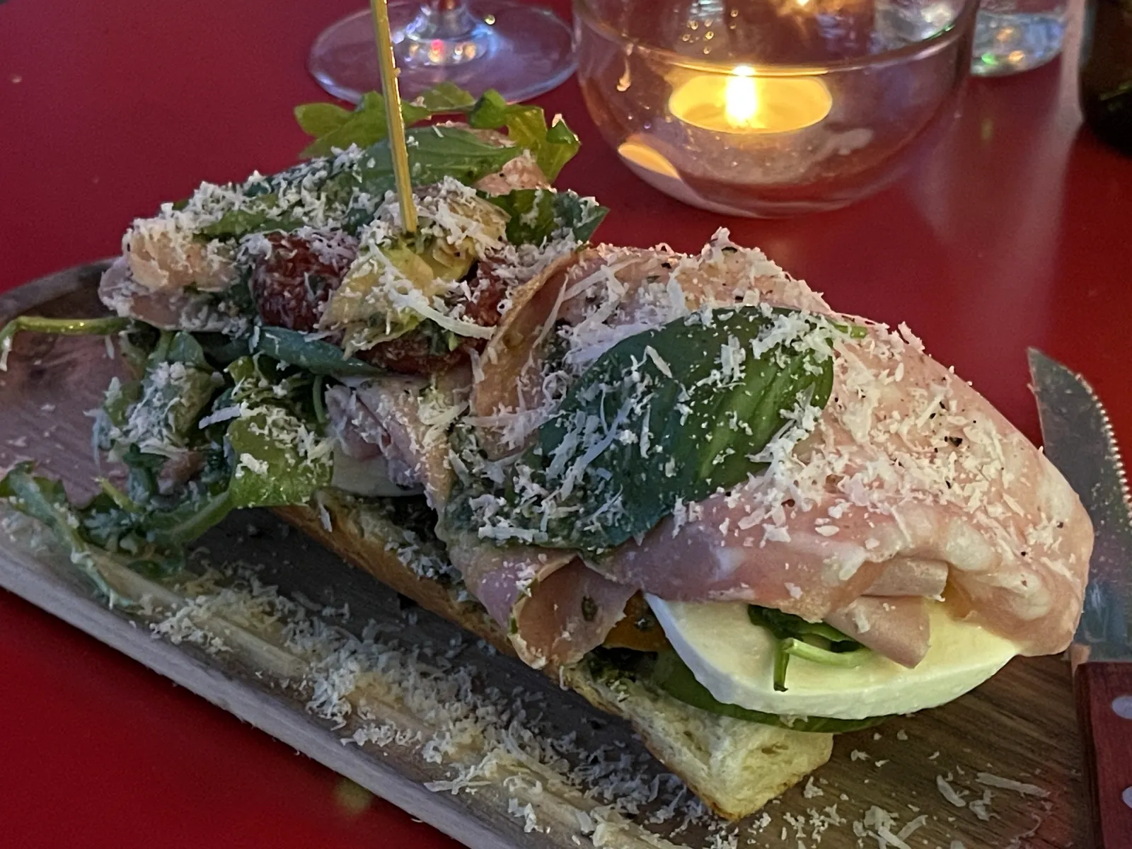 Nahaufnahme eines reich belegten Brotes mit Salat, Schinken und frisch geriebenem Käse bei Amigo's