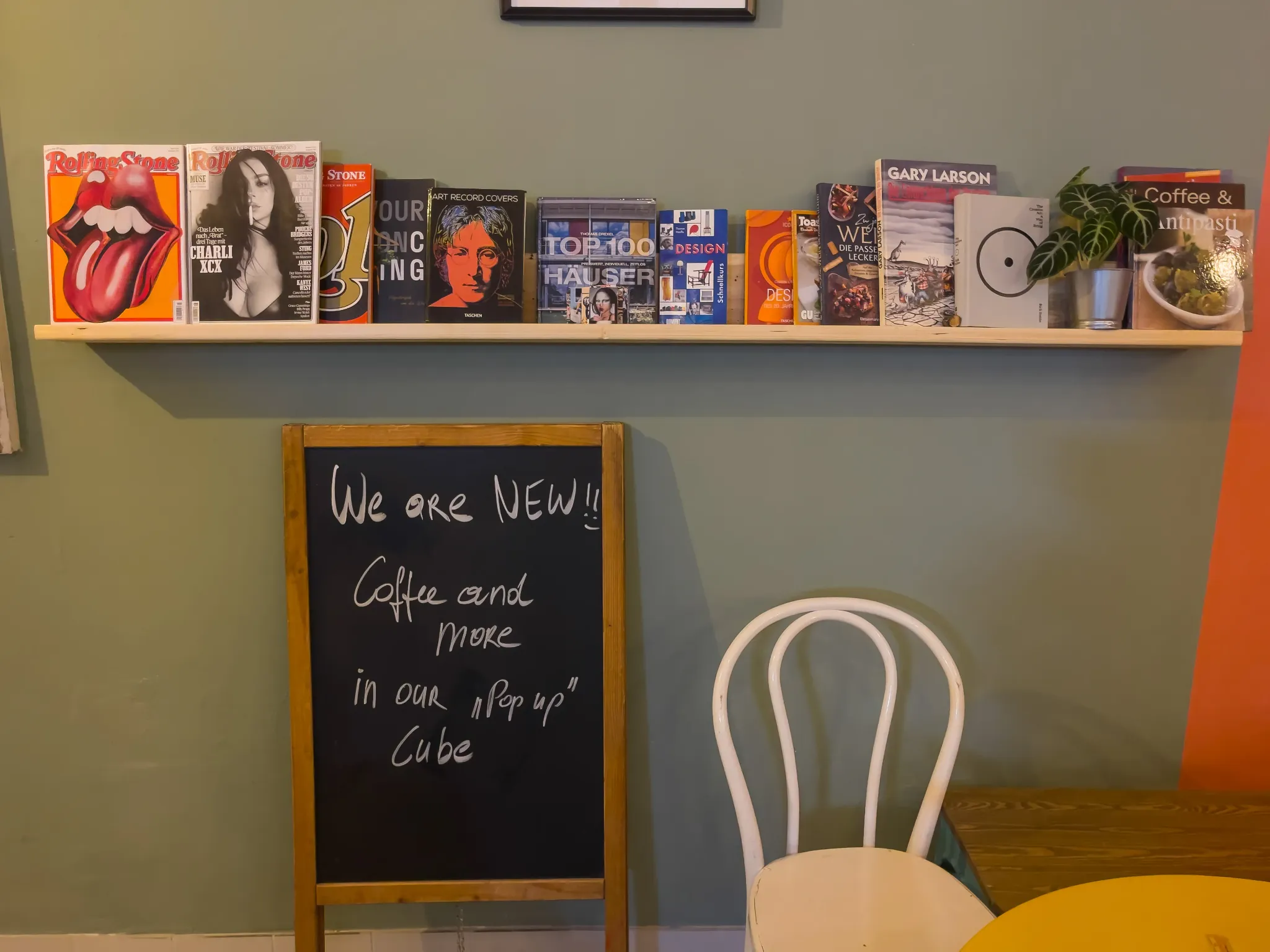 Magazine, Bücher und Designobjekte an einer salbeigrünen Wand