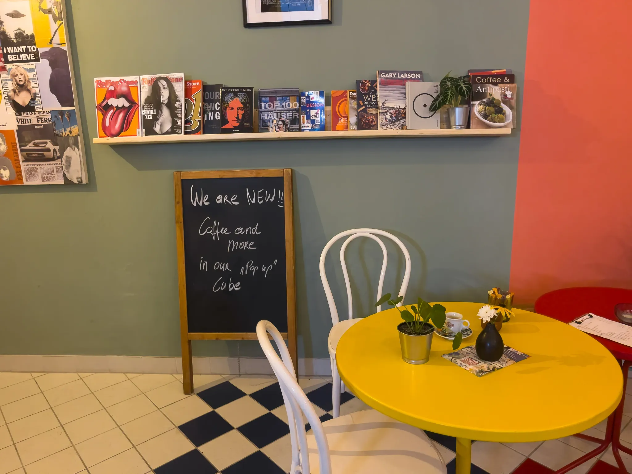 Gelber Tisch, weiße Stühle und eine handbeschriebene Tafel im farbenfrohen Gastraum